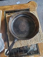 Top view of large round black cast iron pan with handle and side spouts on square natural fiber mat