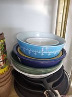 Stack of multiple bowls including a light blue Pyrex bowl with white snowflake pattern on top, darker bowls beneath on shelf.