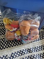 Two plastic bags filled with various parts from Mr. Potato Head toys including heads and limbs, displayed on a patterned rug in front of a large blue plastic bin.