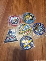 Photo showing six sealed embroidered NASA mission patches on wooden floor, arranged in two rows.