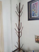 Full front view of the wooden tree coat rack in corner against white walls, showcasing height and multiple hooks.
