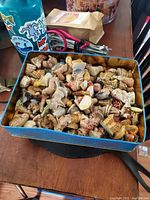Metal tin filled with a large assortment of small painted Wade ceramic figurines, showing various shapes and colors.
