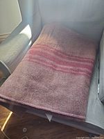 Full view of folded wool blend blanket on chair, showing brown and pink color with horizontal pink stripes.