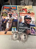 Photo shows two baseball magazines with visible covers and two sealed baseballs in front.
