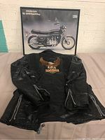 Photo showing the black Goldwing motorcycle jacket with front Honda Goldwing patch, laid flat with sleeves extended, showing damage and zippered cuffs.