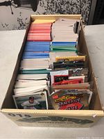 Wide shot showing a box filled with multiple stacks of sports trading cards, mostly rectangular and colorful, with some still in sealed packs.
