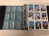 Open binder with nine baseball cards visible on the right and the backs of cards with statistics on the left side held in protective plastic sleeves within a three-ring binder.