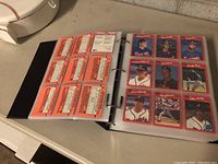 Photo showing open binder with plastic sleeves holding multiple 1990 Donruss baseball cards including player photos and card backs with statistics.