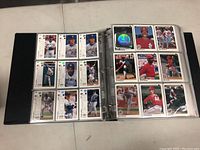Open binder displaying baseball cards on two pages, featuring players from various teams and a holographic card insert.