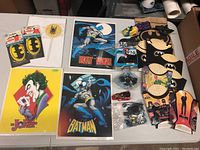 Array of vintage Batman collectibles including McDonald's toys, sandwich bags, black Batman masks, and multiple posters of Batman and The Joker.