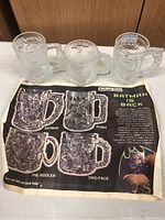 Photo showing all three Batman glass mugs and a Batman-themed placemat with images and descriptions of each character on the mugs.