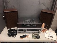 Full view of stereo system, two speakers, headphones, papers, lamp and accessories on grey concrete surface
