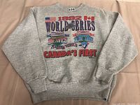 Back of the gray sweatshirt showing large colorful 1992 World Series graphics with American and Canadian flags, team logos, and 'Canada’s First' text.