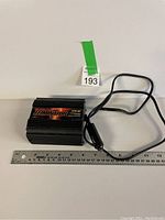 Black 175 watt power inverter with attached cable and car cigarette lighter plug, placed next to ruler for scale.