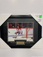 Framed photo of Guy Lafleur skating near the goal, name plate shown.