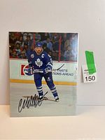 Glossy color 8x10 photo of Wendel Clark in blue Toronto Maple Leafs jersey captured skating. Autograph visible on photo lower half.