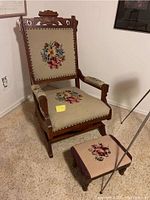 Photo showing full view of the Eastlake style rocking chair with needlepoint floral upholstery on seat, back, and armrests, accompanied by a matching footstool with similar needlepoint upholstery and burgundy trim.