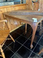 Side view of antique oak table showing carved leg ending in caster, with one chair and two table leaves resting on table.