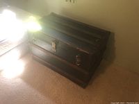 Closed antique steamer trunk showing dark wood and metal latch hardware with visible wear.