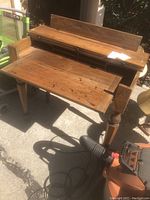 Front and top view of the antique wooden desk showing raised back panel, open hinged main writing surface, and storage compartments.