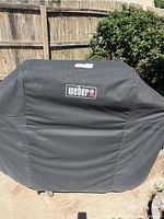 Black Weber branded grill cover on the grill, protecting it from elements.