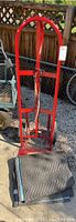 Front view of red truck dolly with strap and black moving blanket on ground in front of it.
