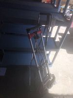 Photo of the two foldable luggage carts leaning against a blue shelving unit, showing their compact folded state and telescoping handles.