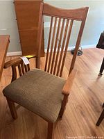 Close-up photo of an oak Mission style arm chair showing vertical slatted back with curved top rail and cushioned brown seat upholstery