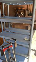Full view of one gray plastic storage shelf with four shelves, placed in a garage with visible tools and other storage items in the background.
