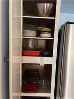 Photo of shelving unit with multiple glass dishes, bowls, and plates showing various sizes and colors including clear glass and orange-red baking dishes.