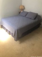 Queen bed with blue-gray quilted bedspread and pillows in a carpeted room.