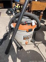 Front and side views of Rigid 2-in-1 blower vacuum showing body, hose, blower nozzle, power cord, and brand labeling