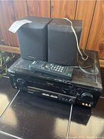 Sony stereo receiver with two Pioneer speakers and remote on black surface, showing dust and wear.