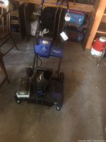 Blue SnoJo hybrid snow blower with battery and charger in a garage setting.