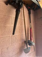 Photo showing black leaf blower, red string trimmer, and metal garden shovel hanging on the garage wall