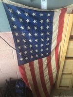 Vintage US flag with 48 stars and stripes hung on a garage wall, showing wear and fabric detail.