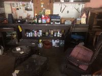 Full view of workbench with shelves and cabinet filled with paint cans, sprays, and containers; pink striped chair in front.