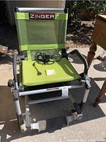 Front three-quarter view of wheelchair showing mesh seat, backrest, and charging cord on seat.