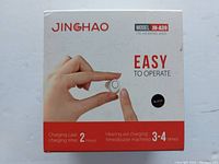 Front side of the product box showing a hand holding the hearing aid, product brand JINGHAO, model JH-A39, black color, charging times information.
