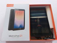 MatrixPad Z1 tablet visible in original branded box with tablet screen reflecting light, and USB cable visible inside box.