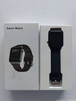 Photo of the smart watch in its retail packaging, showing the watch with a black band next to the box.