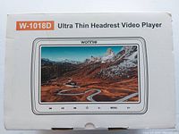 Photo of the front side of the white box with product name W-1018D Ultra Thin Headrest Video Player and an image depicting the screen showing a mountain road.