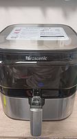 Front view of Proscenic air fryer showing black and stainless steel design, front handle, and illuminated touch button.