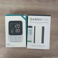 Front view of C02 and QardioArm blood pressure monitor boxes showing device images and model names.
