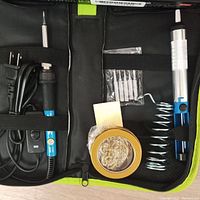 Soldering kit contents including soldering iron, tips, solder wire, stand, and screwdriver in black and green case.