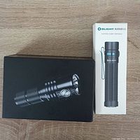 Photo of the boxed Imalent MS03 flashlight next to boxed Olight Warrior Mini flashlight on a wooden surface