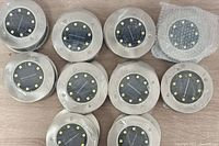 Group of 10 solar puck lights showing the front surface with LED arrangement and solar panel under glass, screws visible on stainless steel top