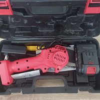 Red cordless mini chainsaw with battery and charger in a molded black plastic carrying case.