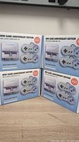 Four factory sealed Mini Game Anniversary Edition consoles with 660 classic games built-in each, showing front of box with console and two wired controllers on display.
