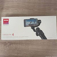Front view of the boxed Zhiyun Smooth 4 smartphone stabilizer showing product image and key features like focus pull, zoom capability, phoneGo mode.